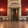 Puertas ornamentadas abiertas a una sala señorial con techos altos, columnas de mármol y empapelada con terciopelo